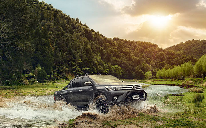 Toyota Hilux crossing a river in a scenic landscape, promoting Kings Rent A Car's rentals.
