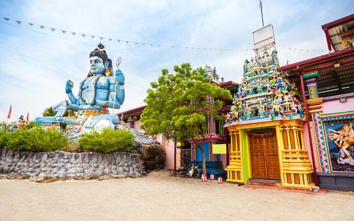 Statue of Lord Shiva beside the vibrant, colorful entrance of Koneswaram Temple in Trincomalee, Sri Lanka